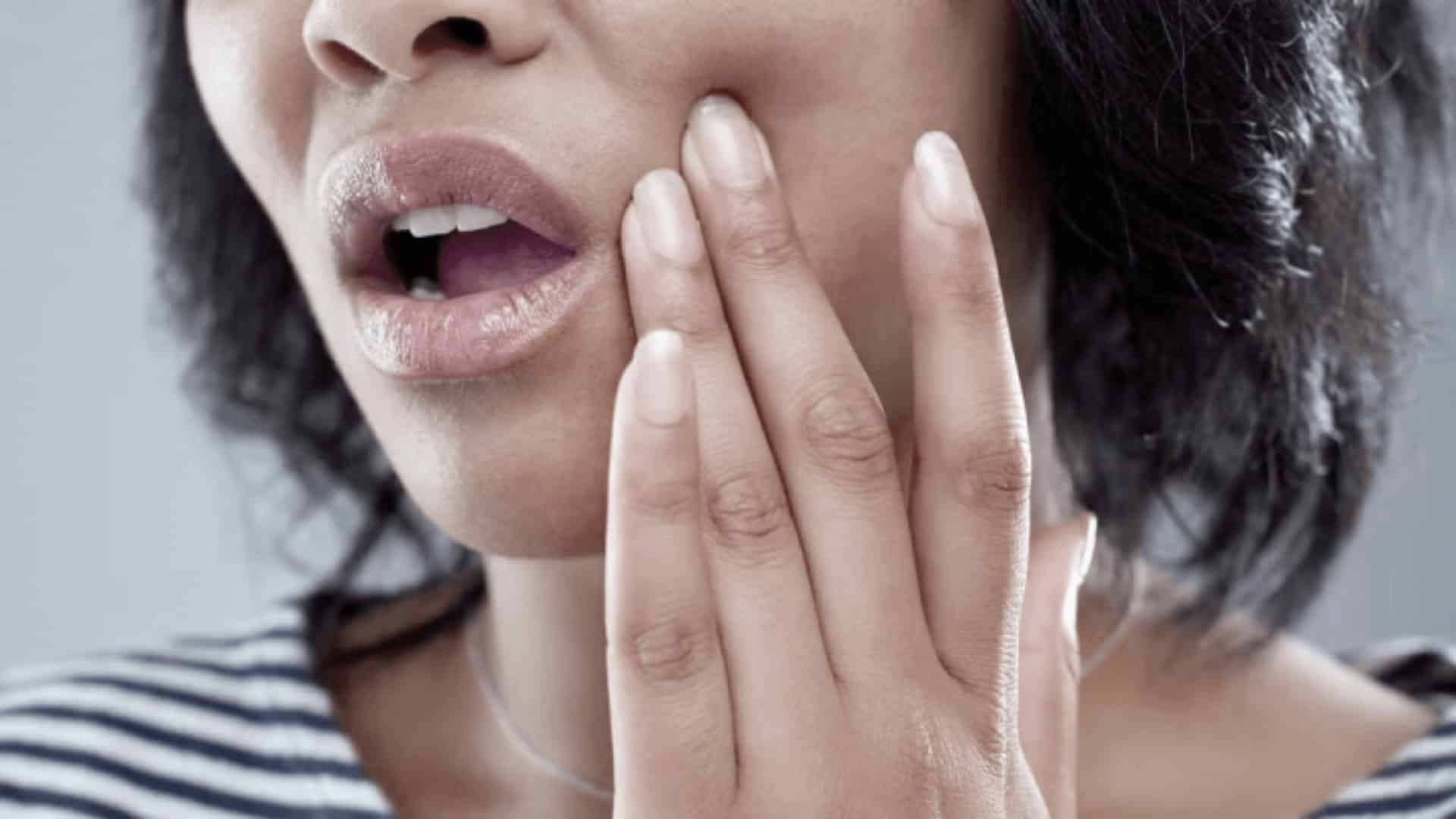 Close-up of woman touching cheek with open mouth, showing jaw pain or tooth discomfort