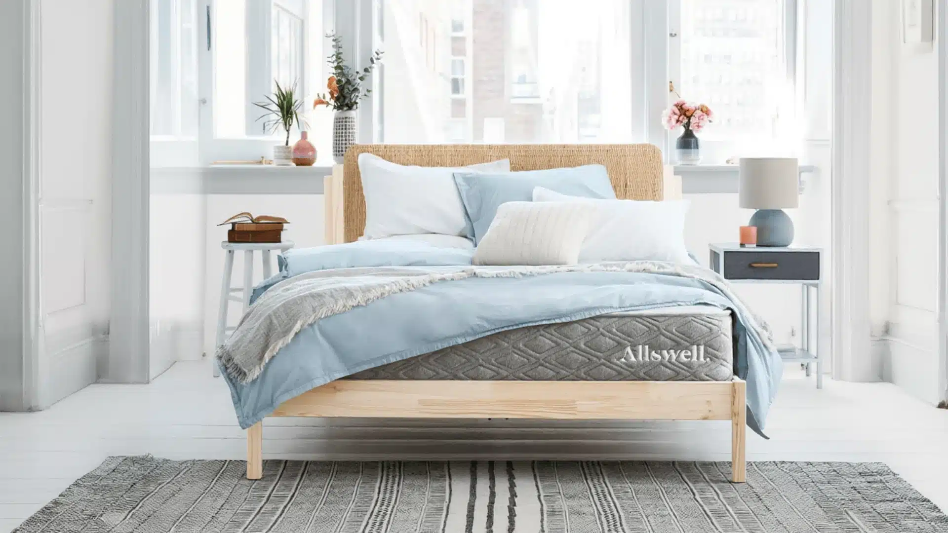 Allswell Luxe mattress on a wooden bed frame in a bright modern bedroom with blue bedding and bedside tables