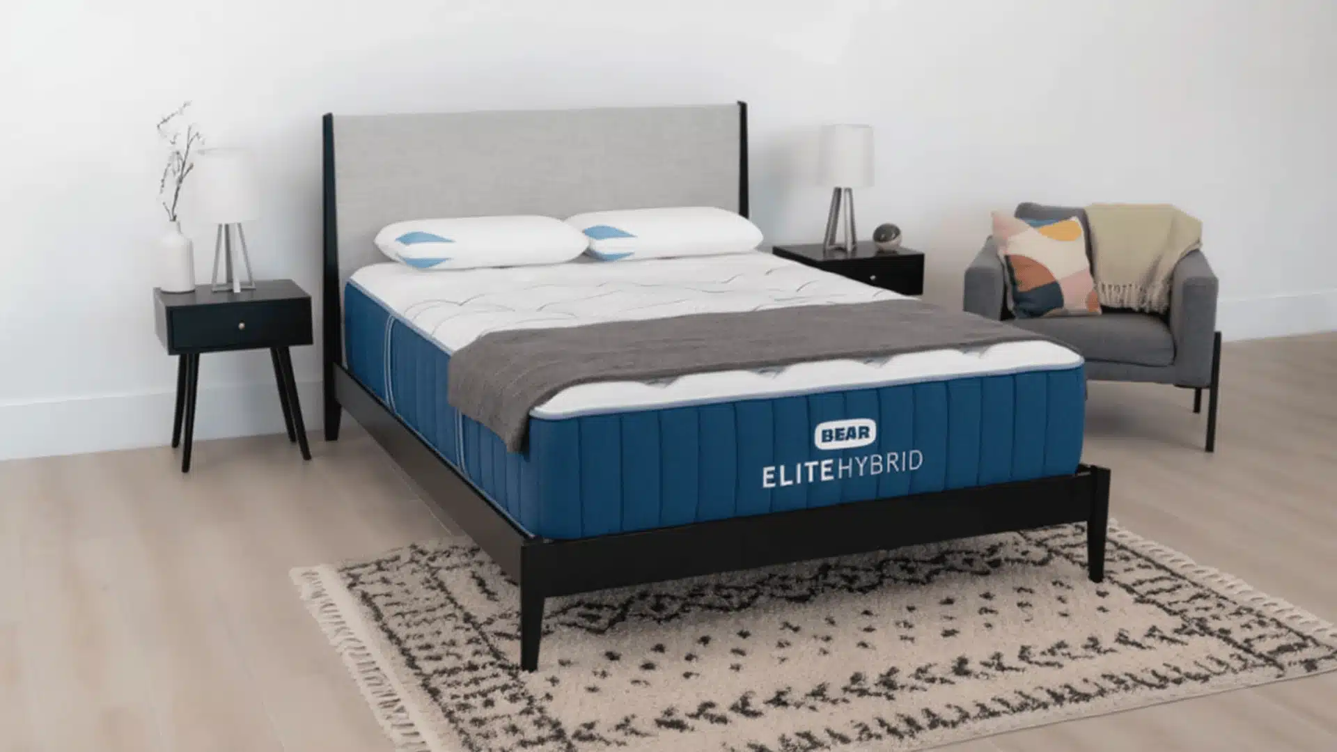 Bear Elite Hybrid mattress displayed on a modern bed with pillows and a gray throw blanket.