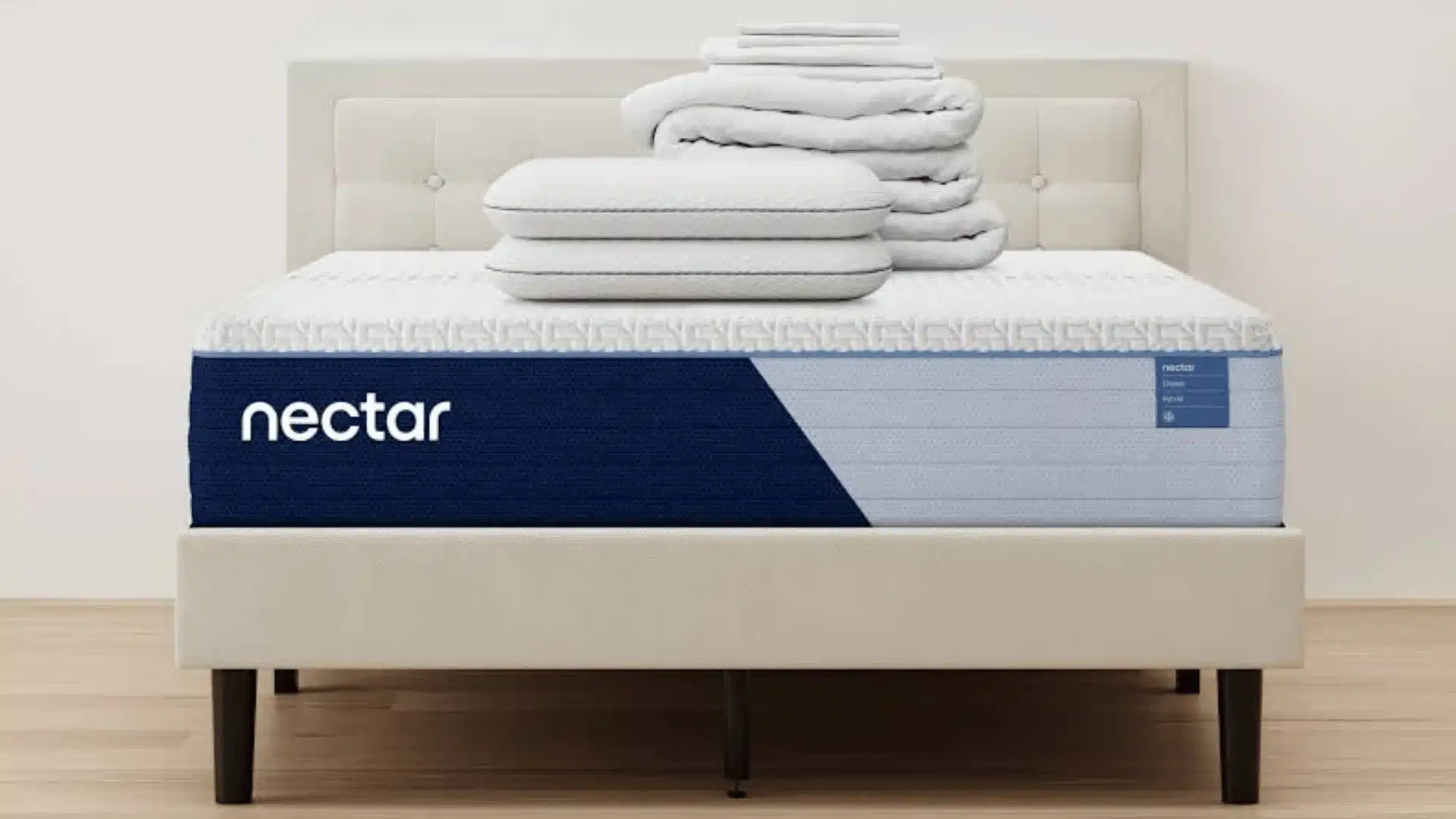 Nectar Classic Hybrid mattress on a beige upholstered bed frame with pillows and folded bedding