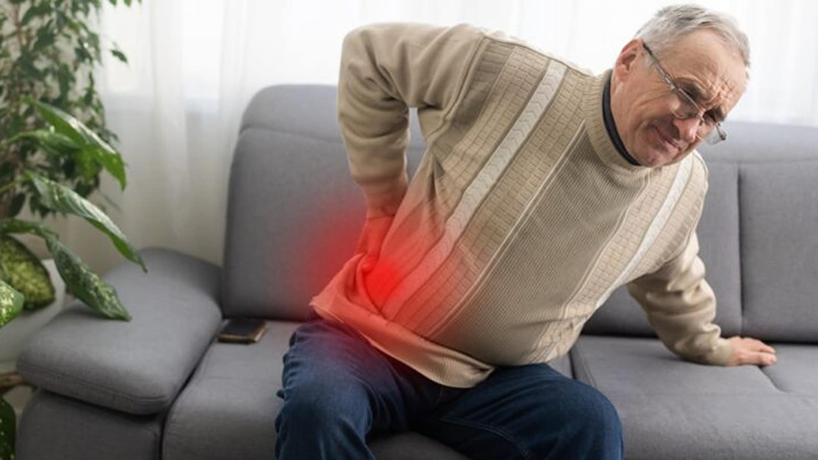 An older man sitting on a couch holding his lower back in pain, with a highlighted area showing discomfort_