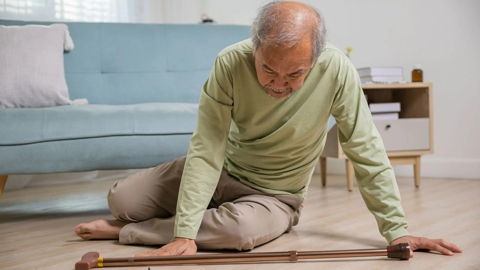 An older man sitting on the floor using a cane for support as he tries to get up in a living room_