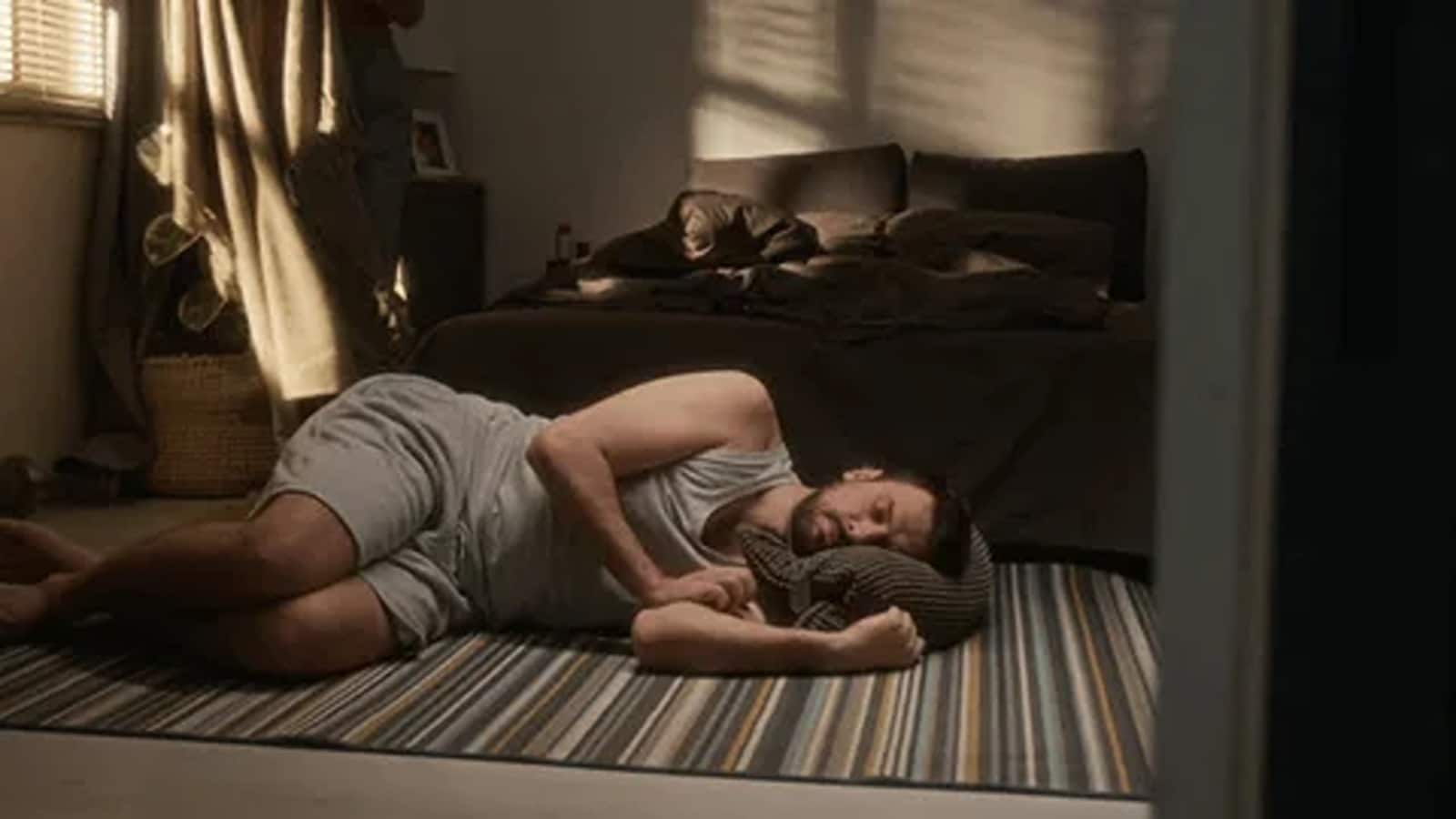 A person lying on their back on a floor mat in a cozy bedroom, with a bed and houseplants in the background, appearing relaxed and comfortable_ (1)