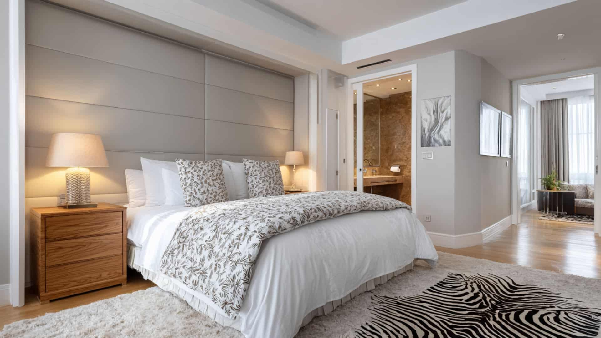 Modern bedroom with large bed, nightstand, rug, and open ensuite bathroom space