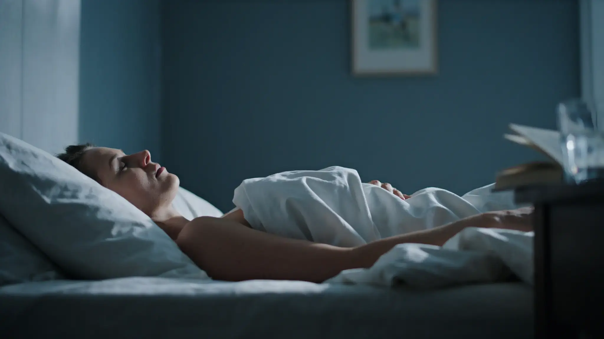A dimly lit bedroom at night with a person sleeping on a white pillow, suggesting restless or disrupted sleep. (1)