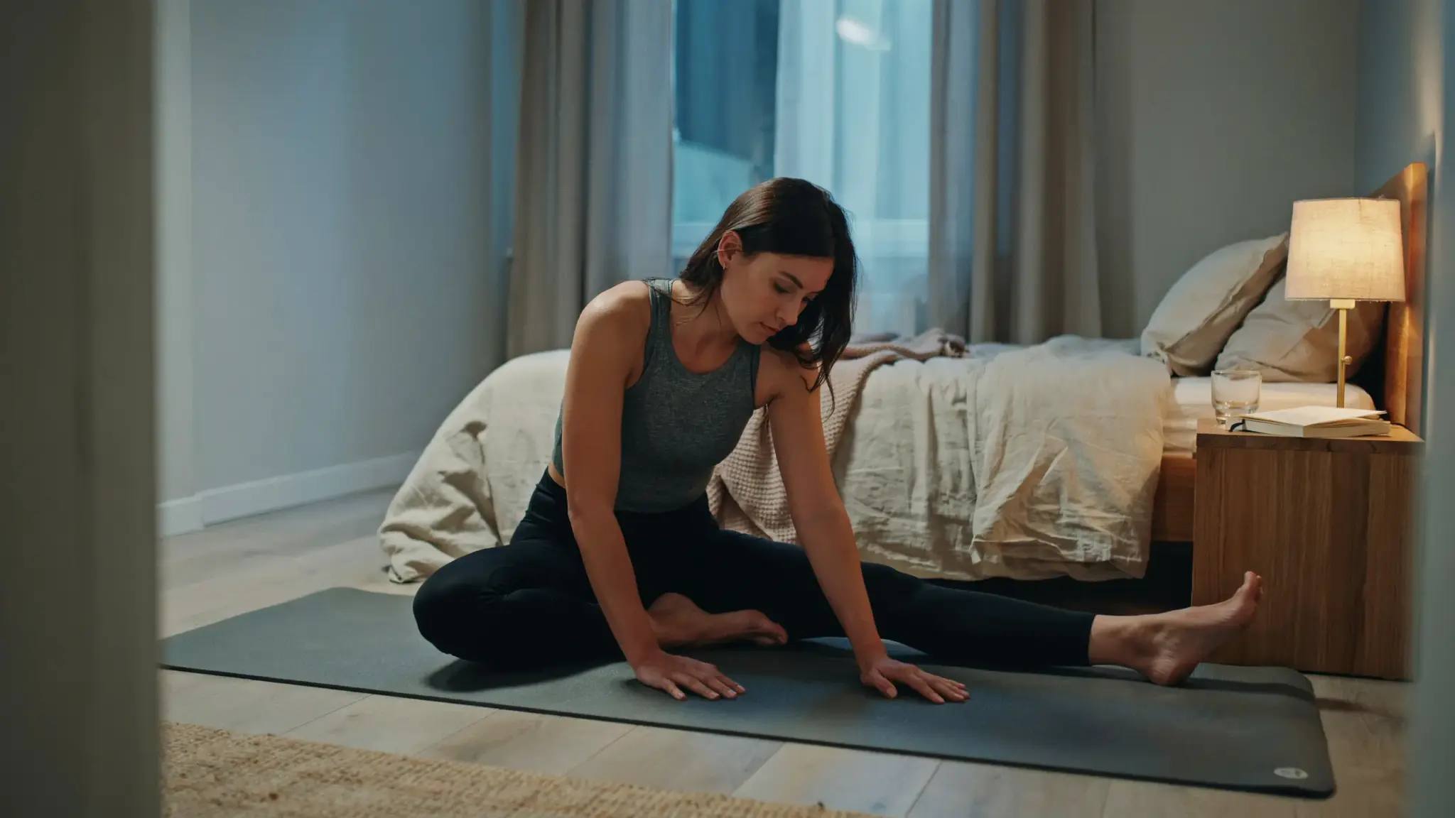 Person doing slow lower body stretches beside bed to release IT band and hip tightness before sleep.