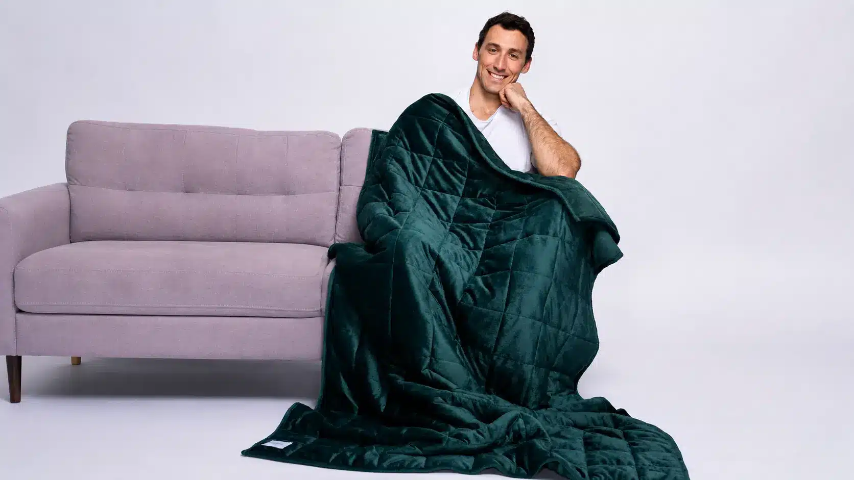 Man smiling on couch wrapped in dark green weighted blanket