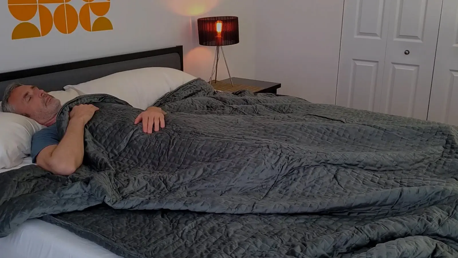Man resting in bed under a textured dark blue weighted blanket