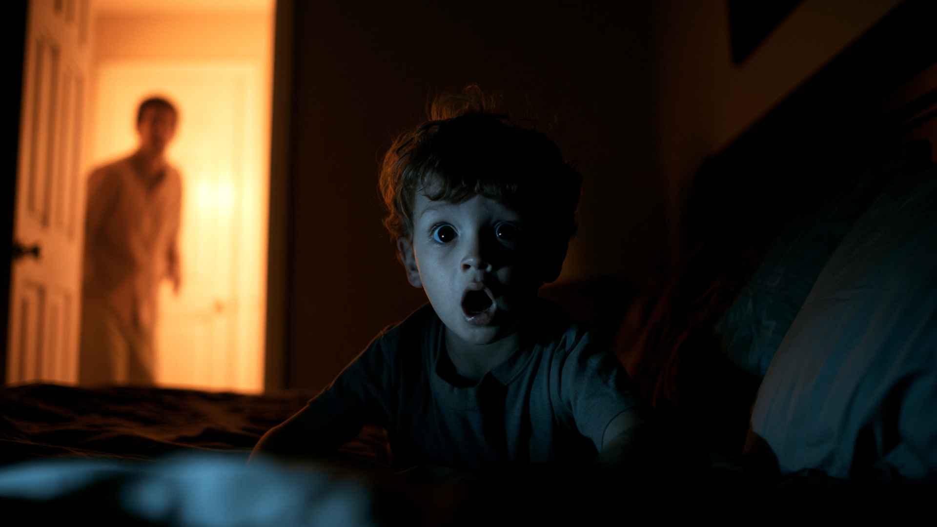Child sitting upright in a dark bedroom during a night terror episode, parent watching helplessly from the lit doorway