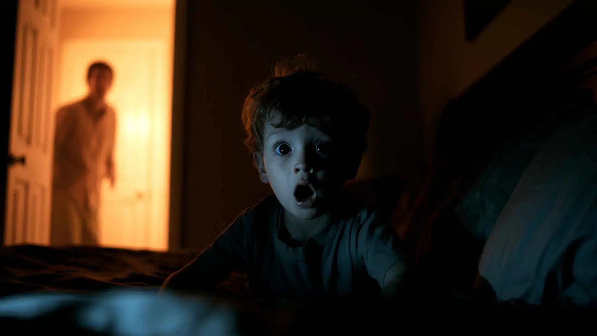 Child sitting upright in a dark bedroom during a night terror episode, parent watching helplessly from the lit doorway