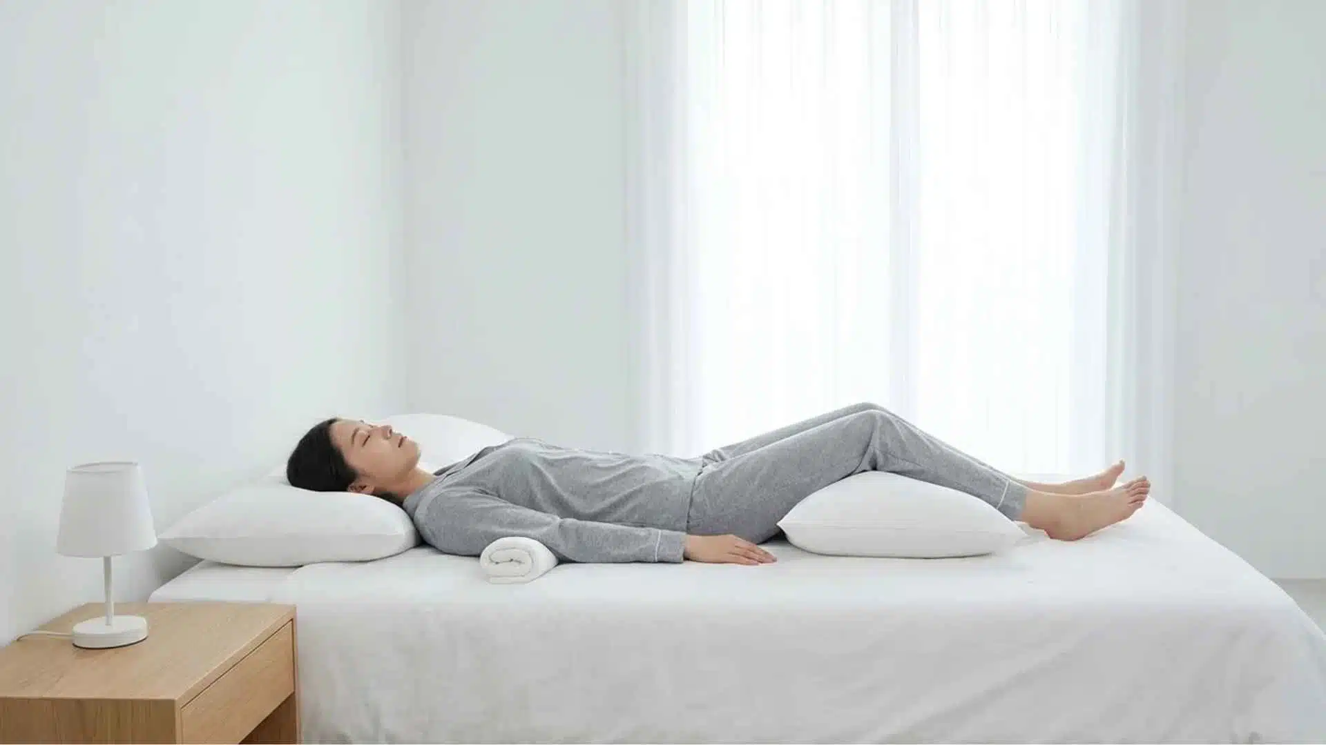 Person sleeping on back with arm supported by pillow and knees elevated reducing shoulder pressure and pain.