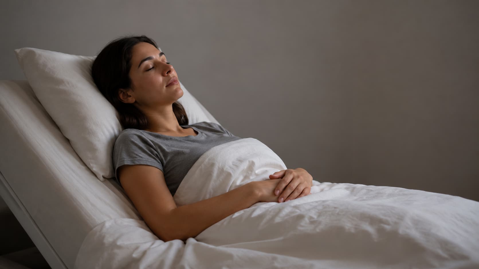 Woman lying on bed with eyes closed, hands folded on stomach, resting with neck supported pillow sleep posture.