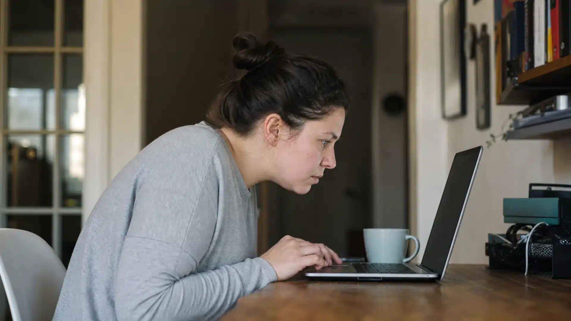 Woman leaning forward with poor posture while working on a laptop at a home desk.