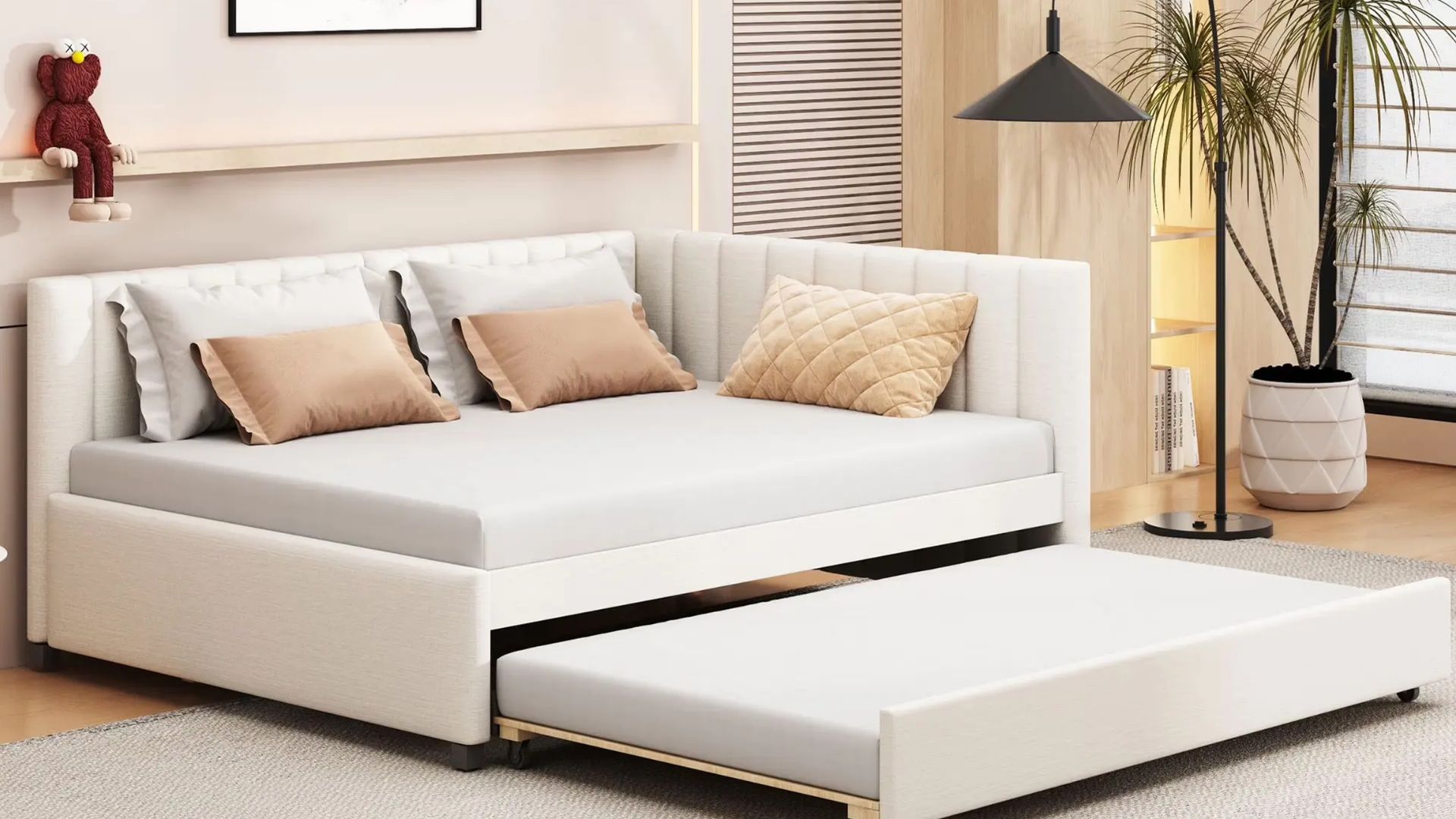 Modern upholstered daybed with a pull-out trundle in a neutral-toned bedroom, with decorative pillows, wood paneling, indoor plants, and a large area rug.