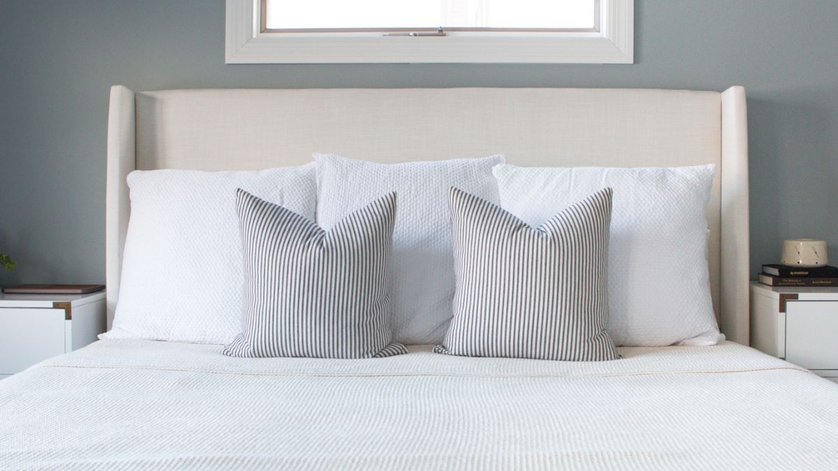 White Euro pillows layered against a cushioned headboard with striped decorative pillows on a neatly styled bed.