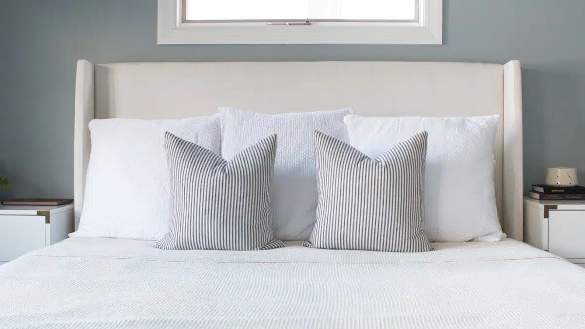 White Euro pillows layered against a cushioned headboard with striped decorative pillows on a neatly styled bed.