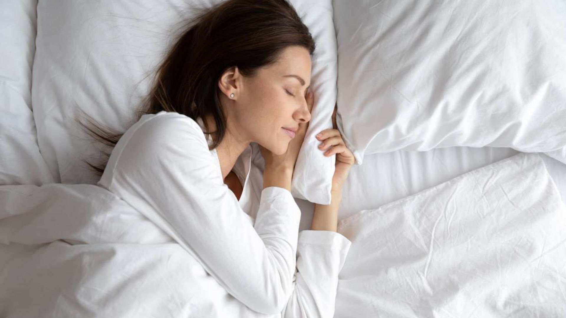 Woman sleeping comfortably on white bedding in a calm bedroom, representing the best sleeping temperature for restful sleep.
