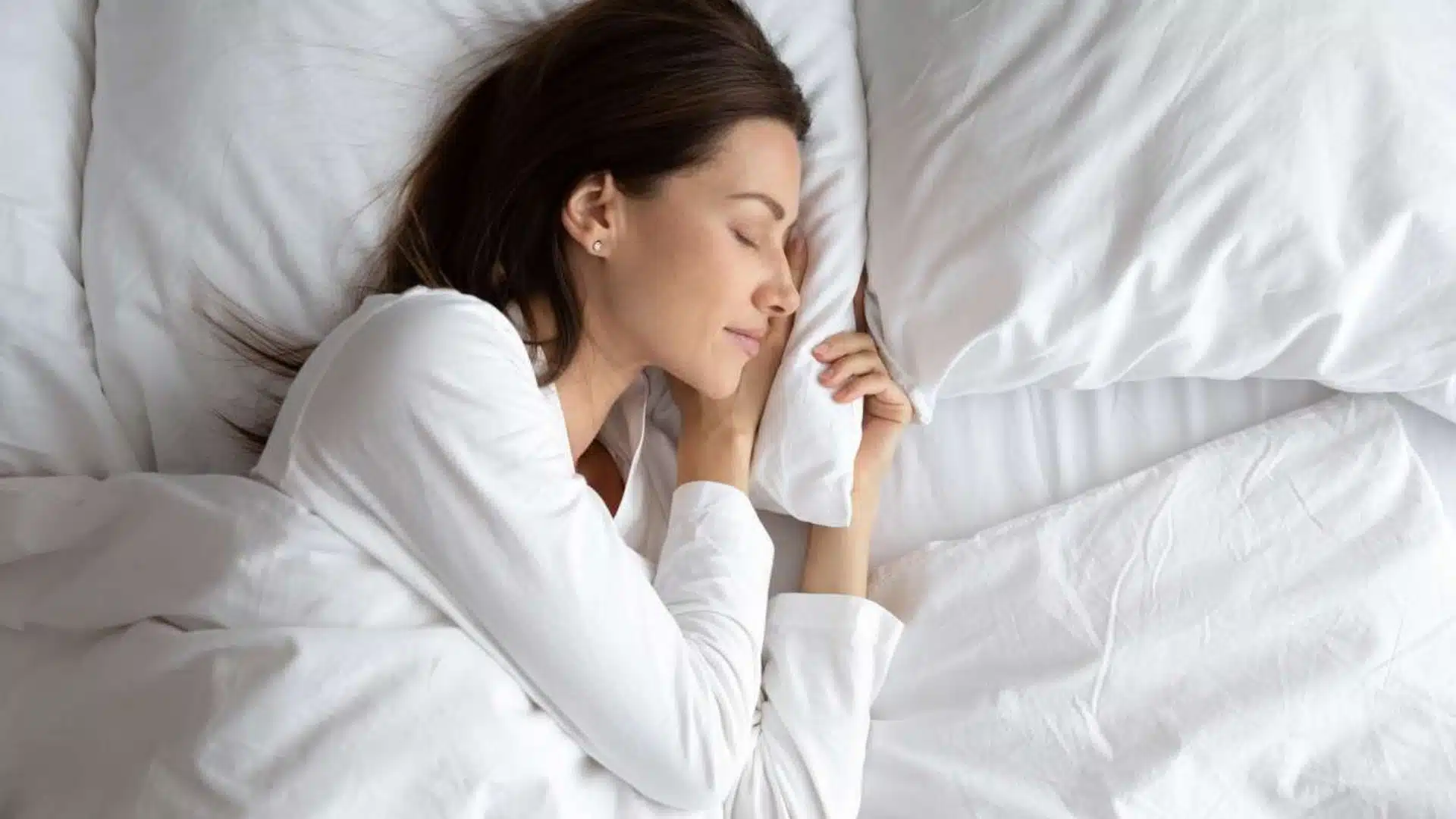 Woman sleeping comfortably on white bedding in a calm bedroom, representing the best sleeping temperature for restful sleep.