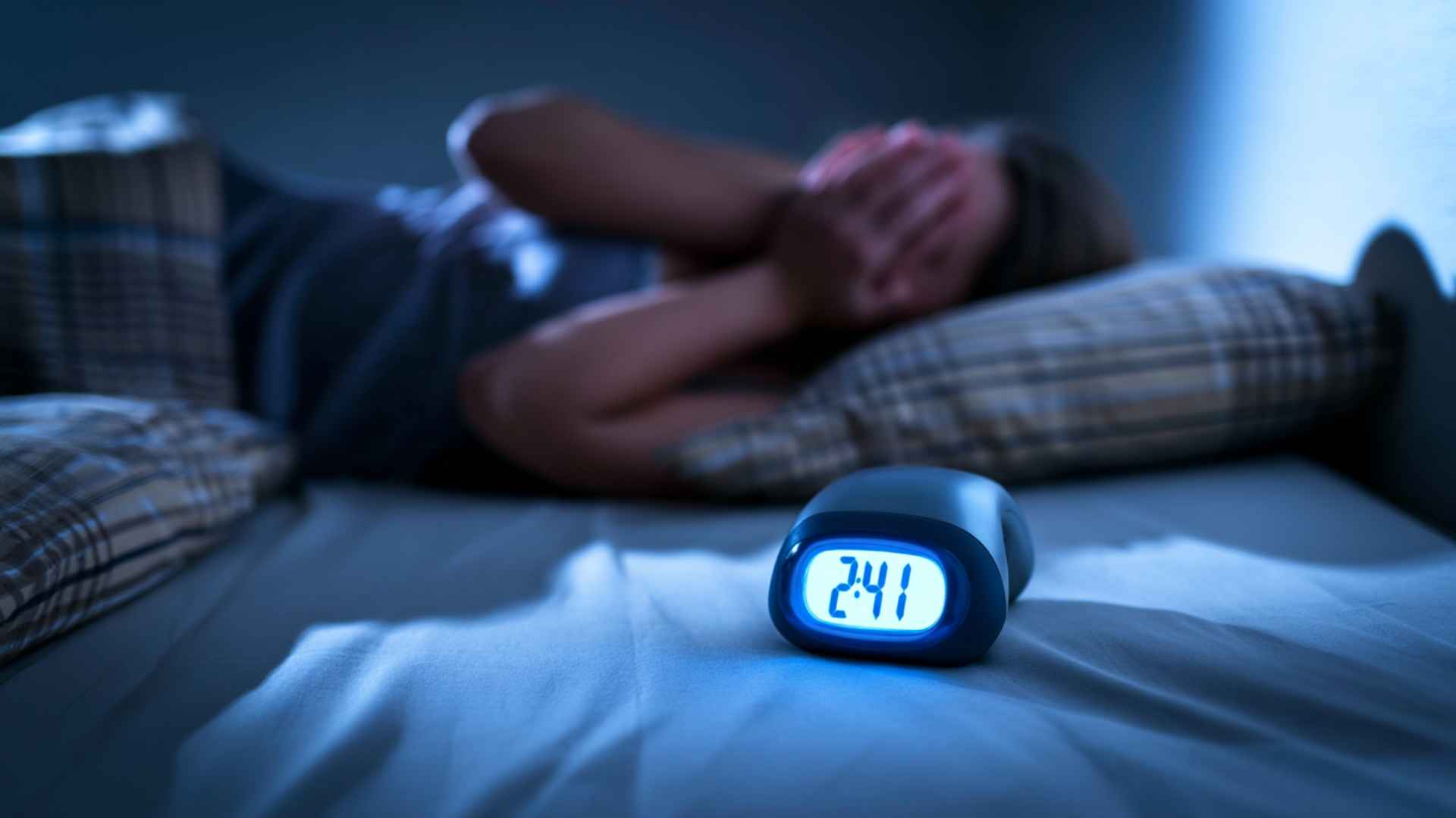 Woman lying awake in bed at night with hands covering her face as a digital clock shows 2:41 a.m