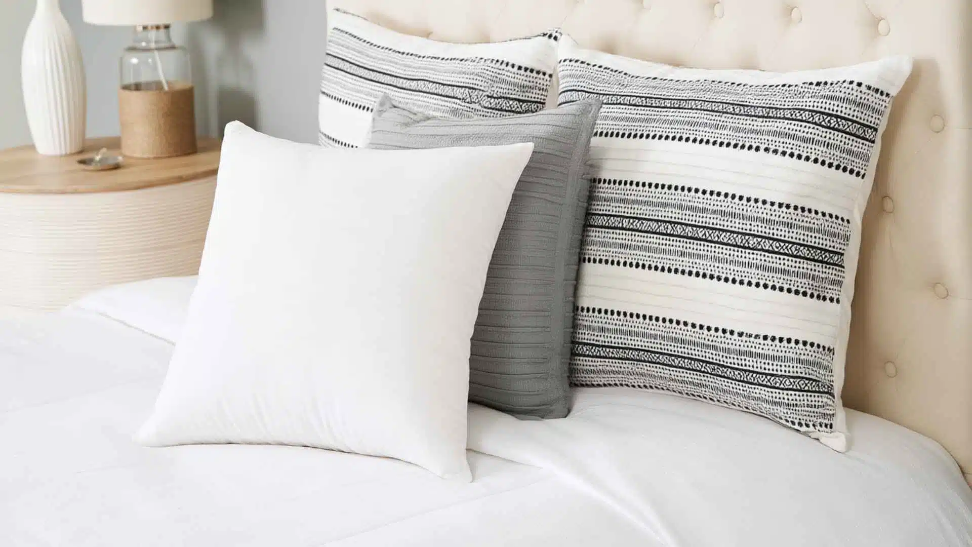 Four Euro pillows in white, gray, and black-and-white patterns arranged against a tufted headboard on a neatly made bed