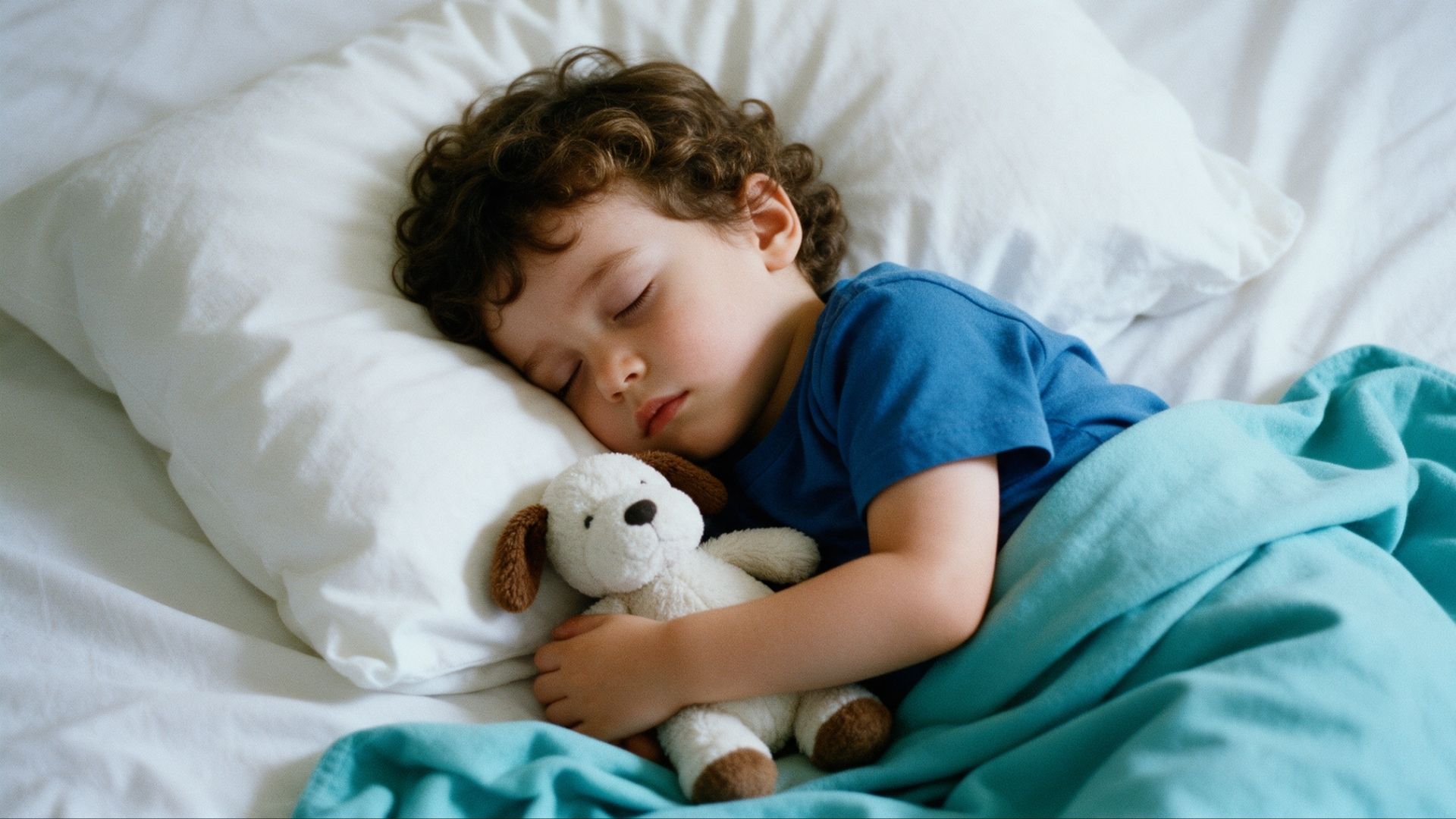 Toddler sleeping peacefully in a bed while hugging a small stuffed toy