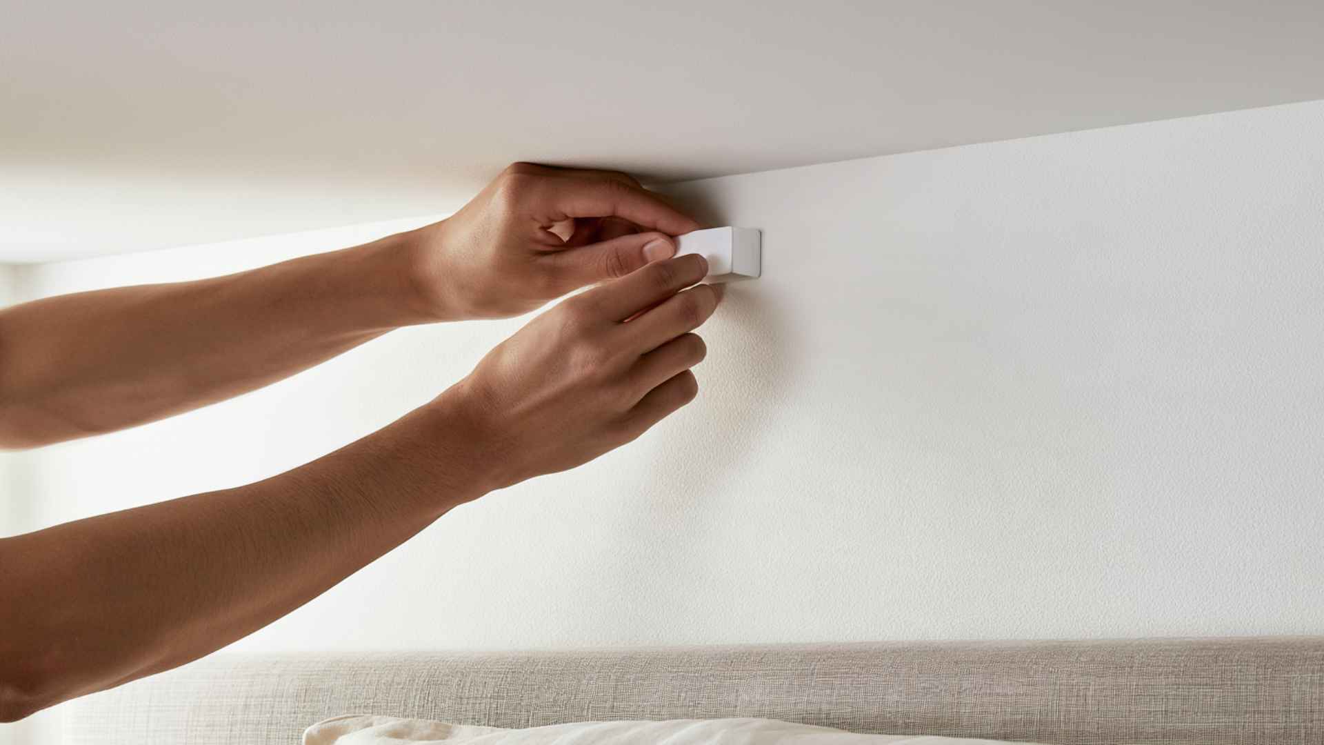 Woman installing a white adhesive ceiling hook above the bed for hanging canopy fabric.