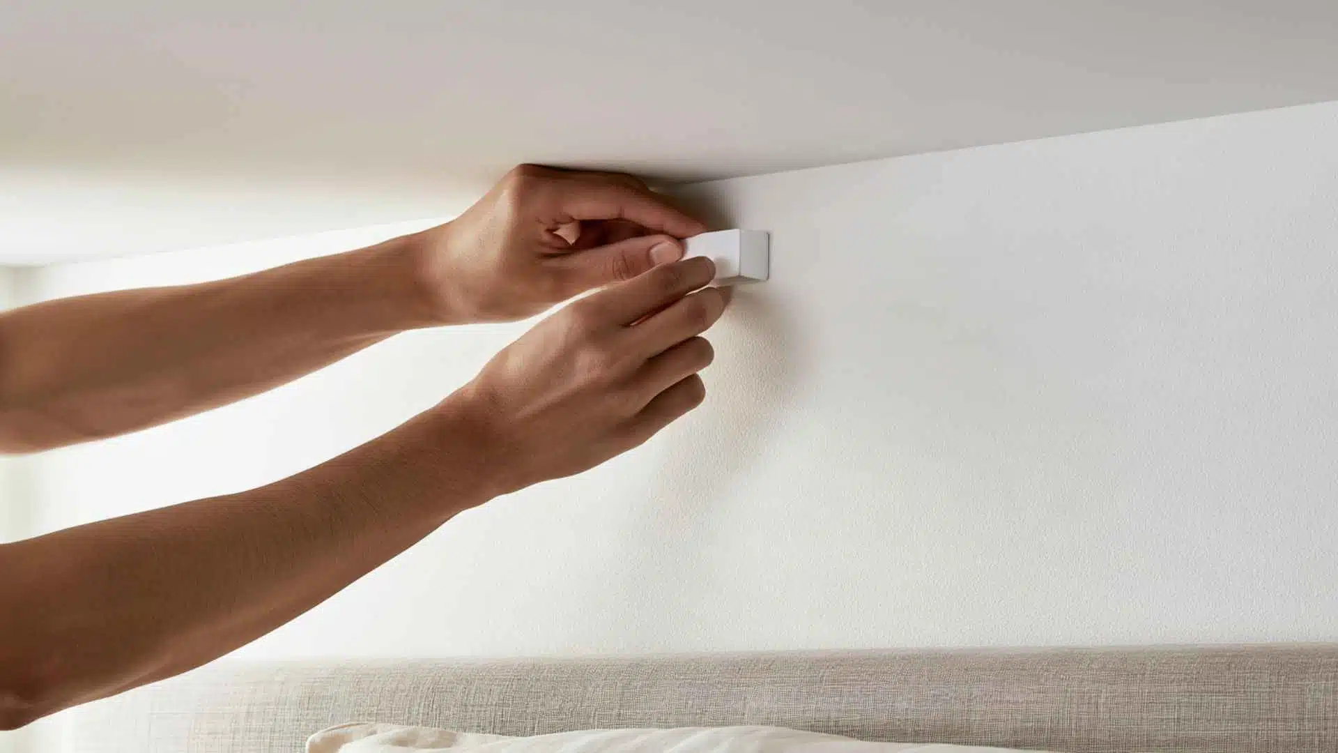 Woman installing a white adhesive ceiling hook above the bed for hanging canopy fabric.