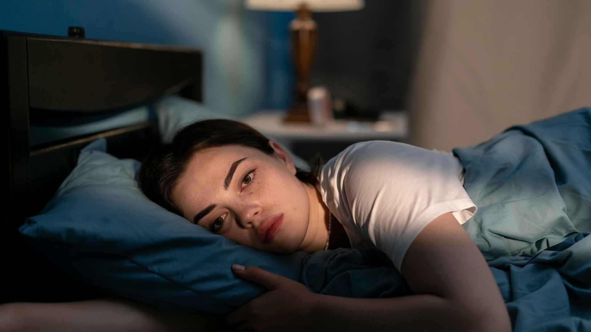 Woman lying awake in bed at night with a worried expression, showing anxiety and difficulty falling asleep
